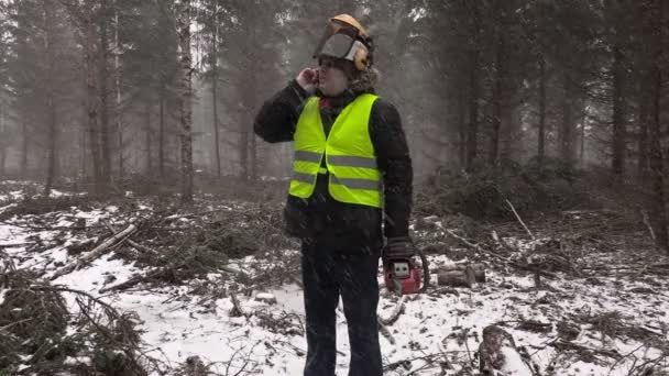 Lumberjack with chainsaw talking on cell phone in heavy snow storm — Stock Video