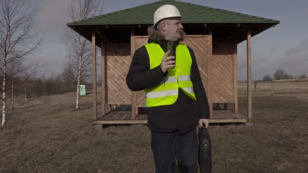 Inżynier budowy, rozmowy na telefon komórkowy w pobliżu drewniany budynek — Wideo stockowe