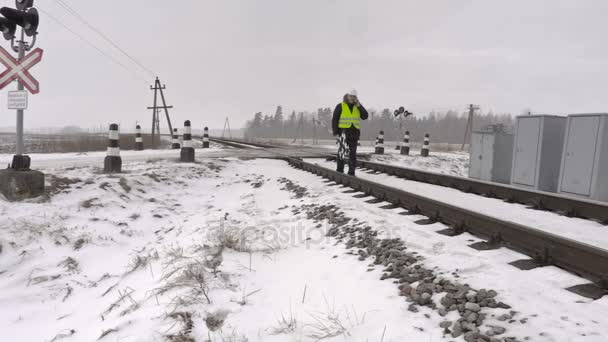 Железнодорожник с предупреждающим знаком разговаривает по телефону и ходит по железной дороге — стоковое видео