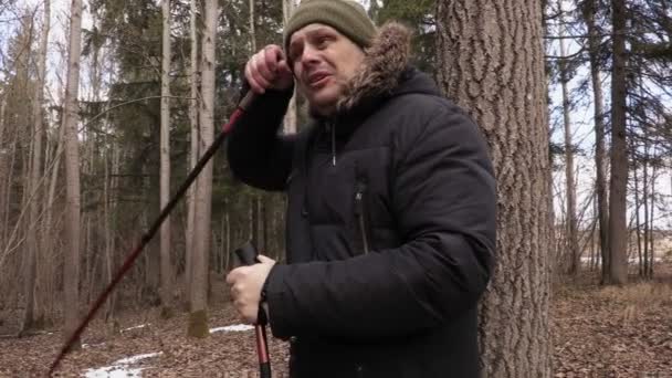 Уставший турист с пешеходными палками возле дерева — стоковое видео