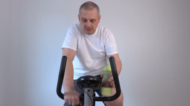 Bir şişe ve kullanılan egzersiz bisikleti içme adam — Stok video