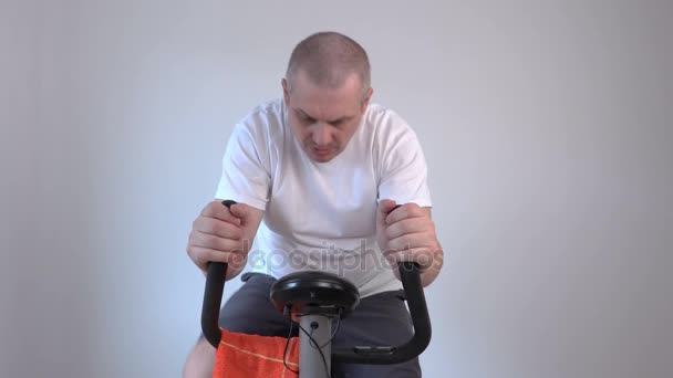 Tired man with a towel on exercise bike — Stock Video