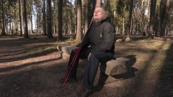 Happy man with hiking sticks on bench in the park — Stock Video