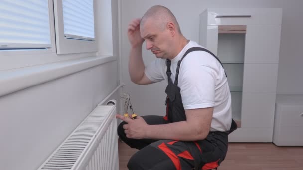 Plumber adjusting radiator and thinking — Stock Video