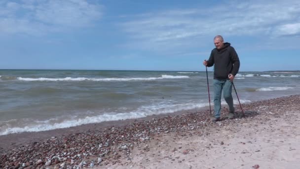 Hombre con bastones de senderismo mantener las manos en la playa cerca del mar — Vídeo de stock