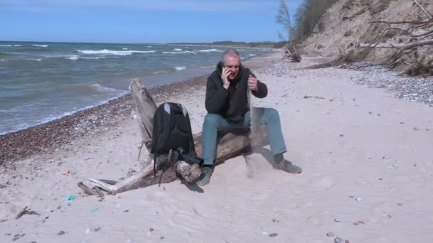 Man zittend op het strand en praten over de telefoon — Stockvideo