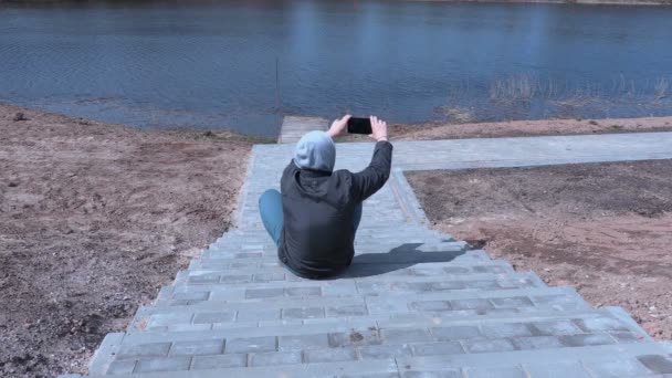 Мужчина сидит на лестнице и фотографирует на планшете — стоковое видео