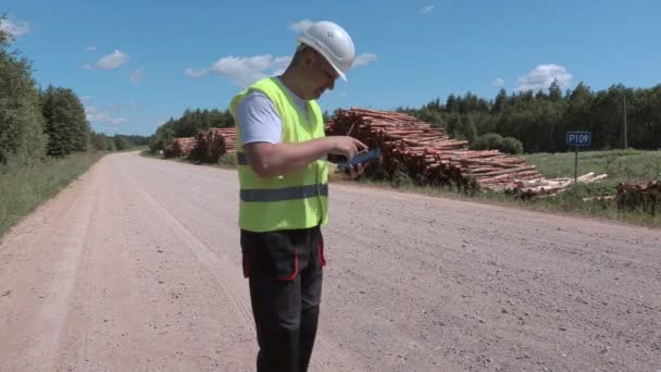 タブレットを使用してログ山近くの道路上の木こり — ストック動画