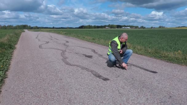 Инспектор использует рулетку рядом со следами шин на дороге — стоковое видео