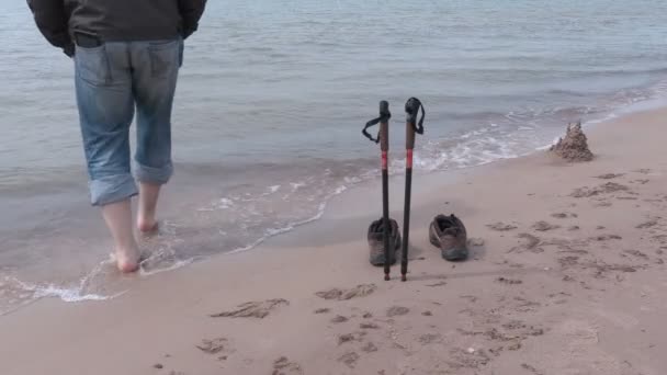 Hombre cerca de bastones de senderismo y el borde del mar — Vídeo de stock