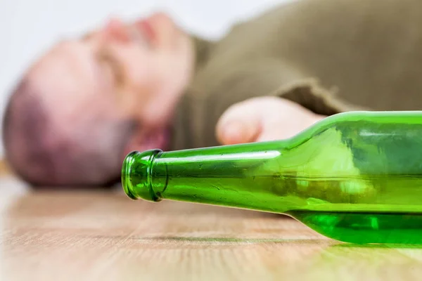 Бутылка перед пьяным мужчиной на полу после злоупотребления алкоголем — стоковое фото