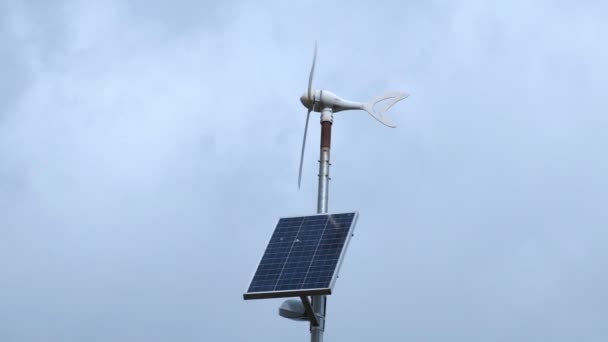 風が強く、曇りの日に太陽電池パネルを備えた風力発電機 — ストック動画