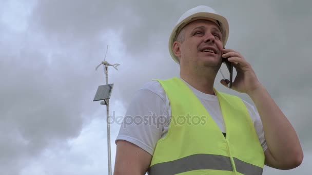 Ingenieur praten over slimme telefoon in de buurt van windgenerator met zonnepaneel — Stockvideo