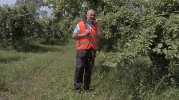Huerto con tijeras de jardinero hablando por teléfono cerca del manzano — Vídeo de stock
