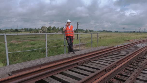 Railway worker on walkie talkie checking rails and walking away — Stock Video