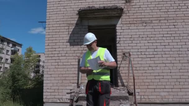Строитель выходит из здания и проверяет территорию — стоковое видео