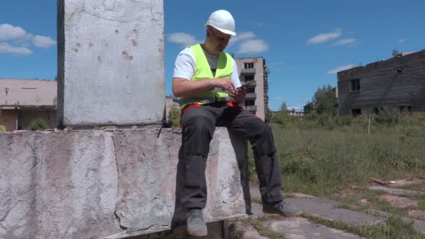 Costruttore stanco seduto vicino a condomini abbandonati e utilizzando tablet — Video Stock