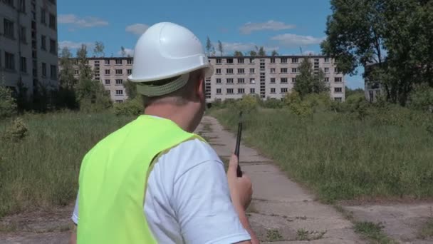 Construtor em walkie talkie caminhando lentamente perto de edifícios — Vídeo de Stock