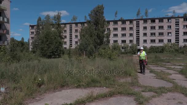 Bauarbeiter mit Walkie-Talkie läuft in der Nähe verlassener Mehrfamilienhäuser — Stockvideo