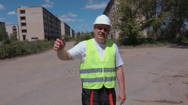 Будівельник розмовляє з гостями біля покинутих багатоквартирних будинків — стокове відео