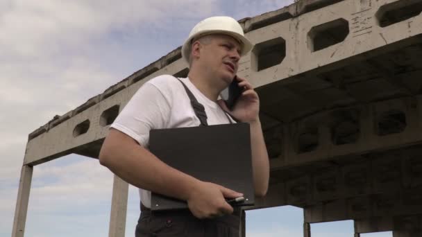 Ingénieur parlant sur un téléphone intelligent près d'un bâtiment inachevé — Video