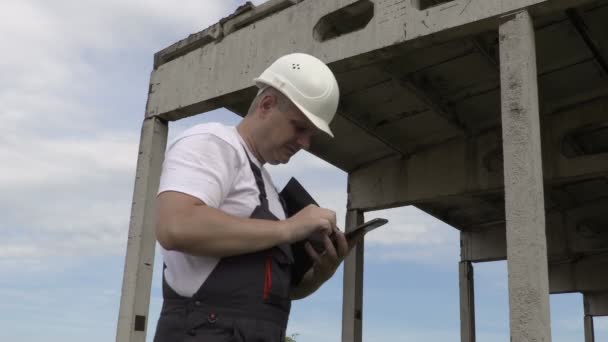 エンジニアは、未完成の建物の近くのスマート フォンで写真を撮る — ストック動画