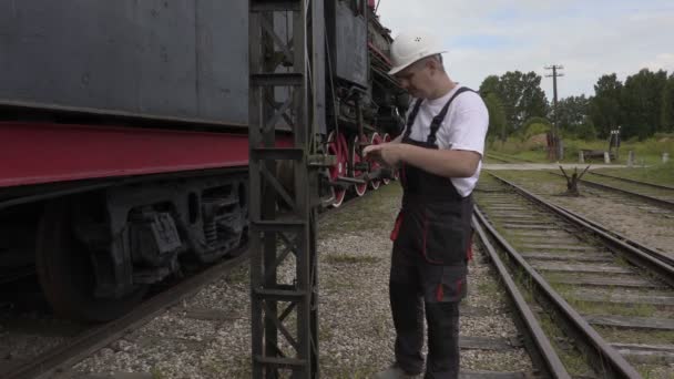 Сотрудник железной дороги фотографирует на смартфоне рядом с локомотивом — стоковое видео