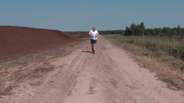 Мужчина бежит по сельской дороге летом — стоковое видео