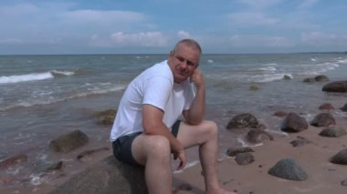 Deniz kıyısı, taş üzerinde oturan yalnız adam