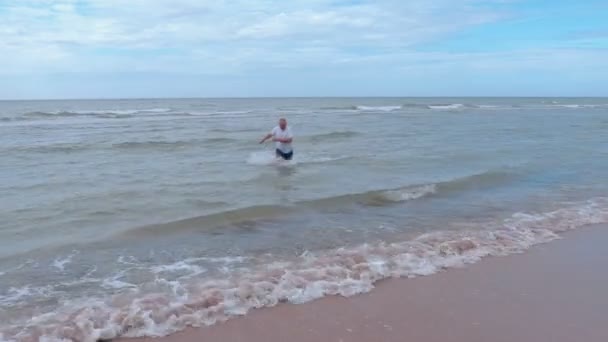 Mann mit nassem T-Shirt kommt aus dem Meer — Stockvideo
