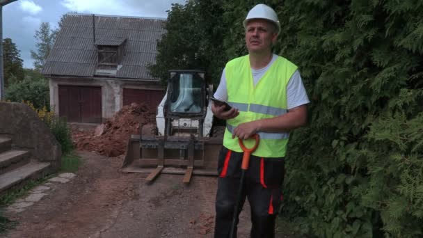 Constructor con pala y tableta cerca del tractor — Vídeos de Stock