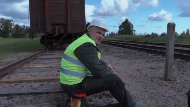 Zklamaný železniční dělník s tabletem, sedí na kolejích — Stock video