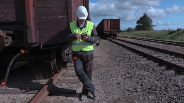 Сотрудник железной дороги на рации и планшетных ПК возле вагонов — стоковое видео