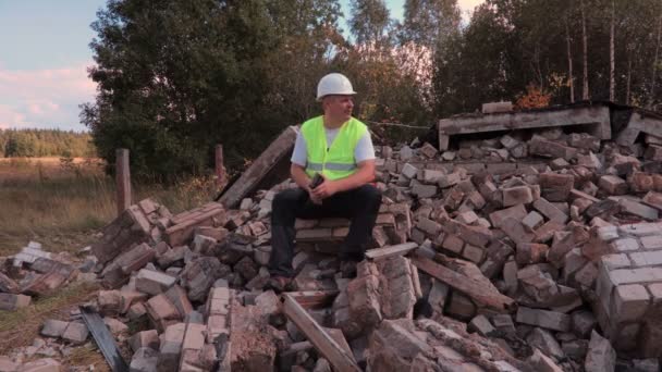 Construtor senta-se na pilha de tijolos e usando tablet PC — Vídeo de Stock