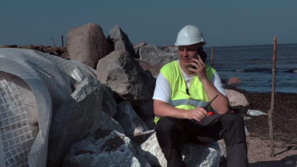 Bouwer praten over telefoon in de buurt van geïsoleerde stenen van pier — Stockvideo