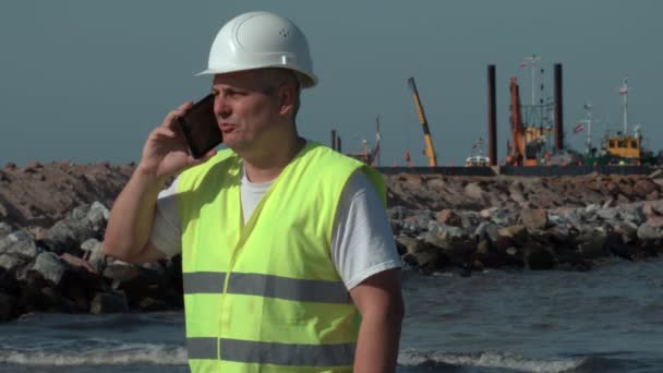 Ingeniero habla por teléfono inteligente en la playa — Vídeo de stock