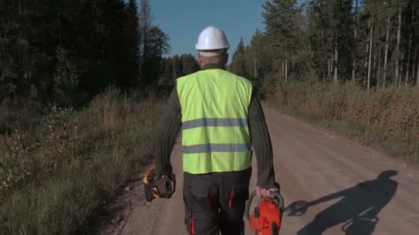 Lesní dělník chůzi na cestě s motorovou pilou — Stock video