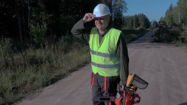 Trabajador forestal en la carretera con motosierra cerca de abeto roto y caído — Vídeo de stock