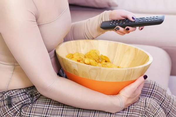 Woman with TV remote control and bowl by chips