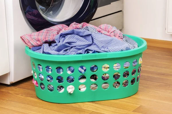 Laundry basket in green color with clothes on the floor at the washing machine