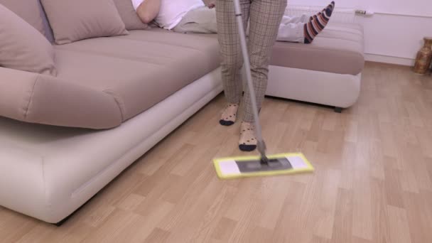 ソファの上のビールで怠け者の近くの床を掃除の女性 — ストック動画