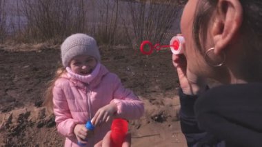 Anne ve küçük kızı parkta sabun balonları patlatmak