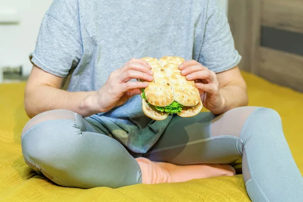 女人坐在床上拿着三明治 — 图库照片