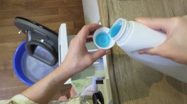 Kadın plastik bardağı çamaşır deterjanıyla dolduruyor.