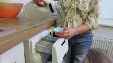 Kadın çamaşır makinesini çamaşır deterjanıyla dolduruyor.