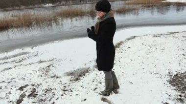 Kışın göl kenarında akıllı telefondan fotoğraf çeken bir kadın.