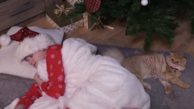 Pijamalı küçük kız Noel arifesinde ağacın yanında uyuyakaldı.