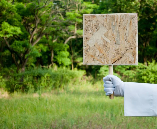 Garsonun el Beyaz eldiven ve beyaz peçete ile ahşap kare tablet veya afiş bir arka plan bulanık yeşil çalılar ve çim üzerinde tutar