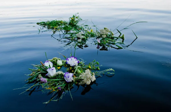 Three beautiful large bouquet of wreaths of white purple yellow beautiful fresh wildflowers and green grass floating along the Ukrainian river Dnieper along the calm water for the feast of Ivan Kupala