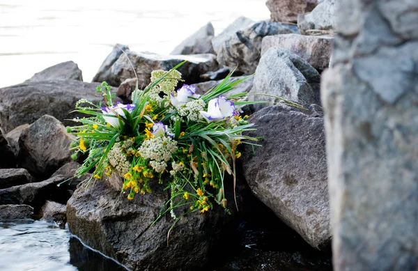 One beautiful large bouquet of a wreath white purple yellow beautiful fresh wildflowers and green grass lies on rocks against the background of the Ukrainian river Dnieper on the feast of Ivan Kupala